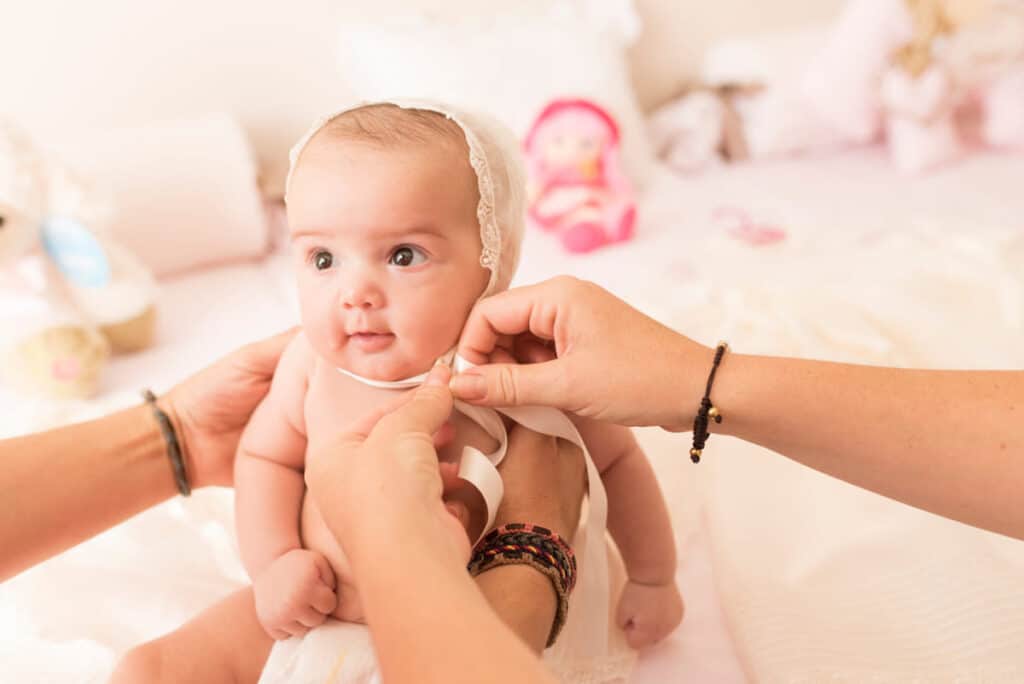 Father and mather clothing baby with christening ceremonial cap