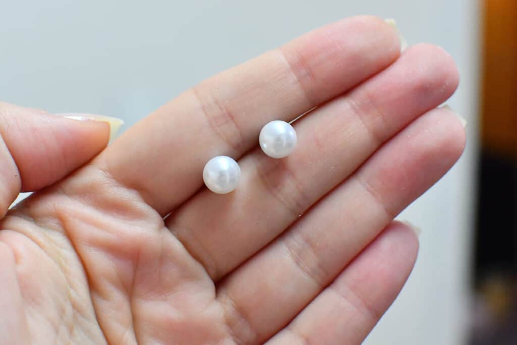 Female hand holding white colored freshwater pearl earring studs