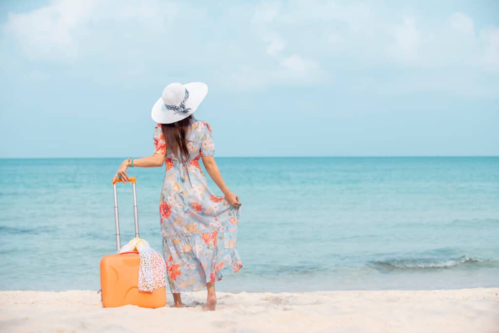 Relax traveler woman in dress with sun hat holding suitcase standing on the beach enjoys her tropical vacation , lifestyle holiday travel summer concept